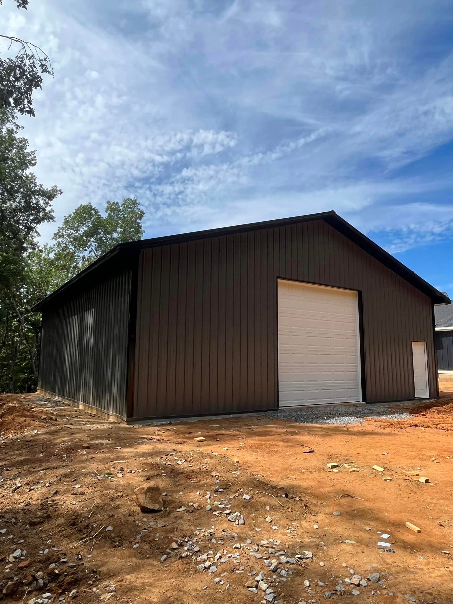 A large metal building with a white garage door is sitting in the middle of a dirt field.