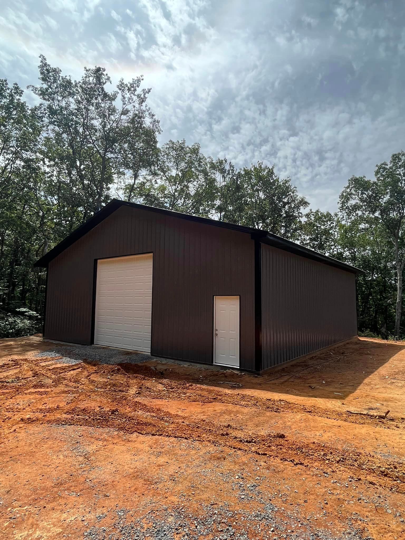 A large metal building with a white garage door is sitting in the middle of a dirt field.