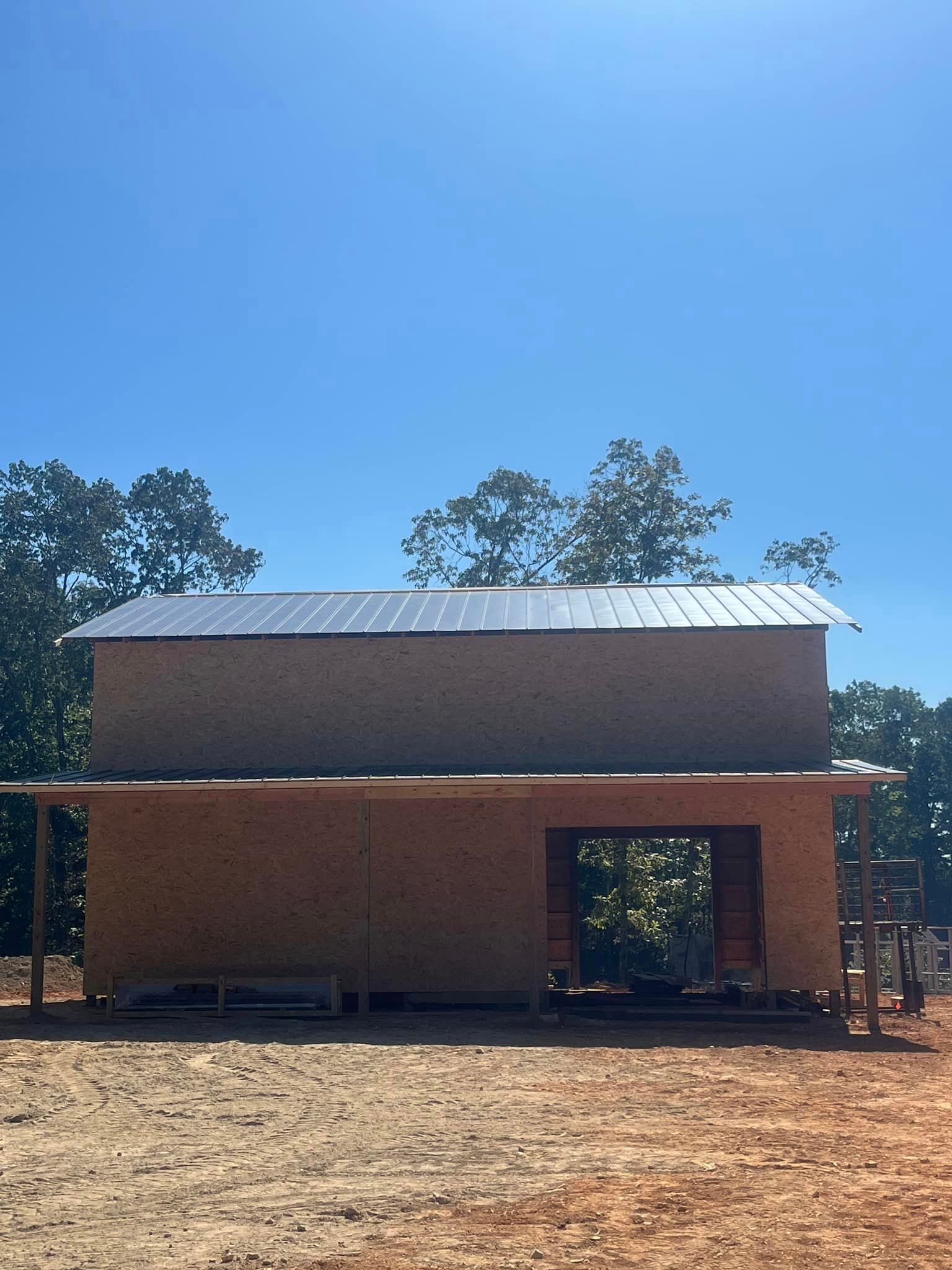 A wooden building with a metal roof is sitting in the middle of a dirt field.