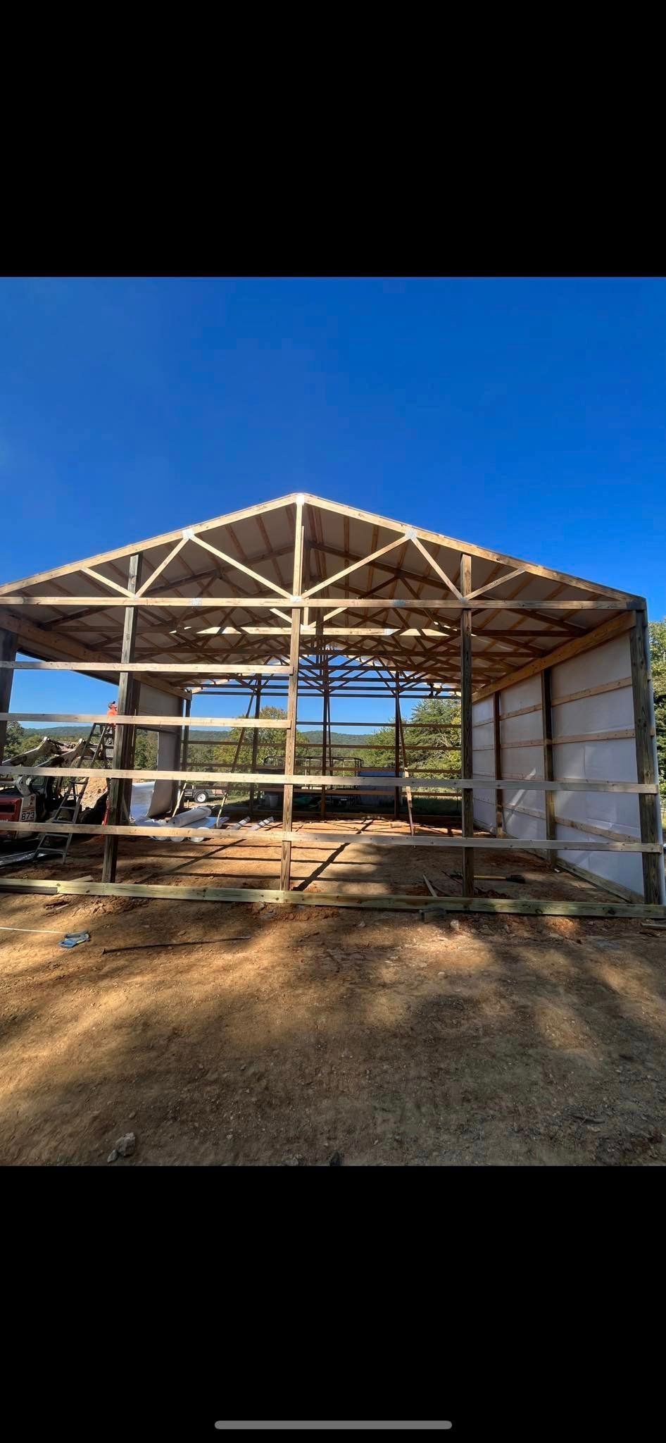 A barn is being built on a dirt field with a blue sky in the background.