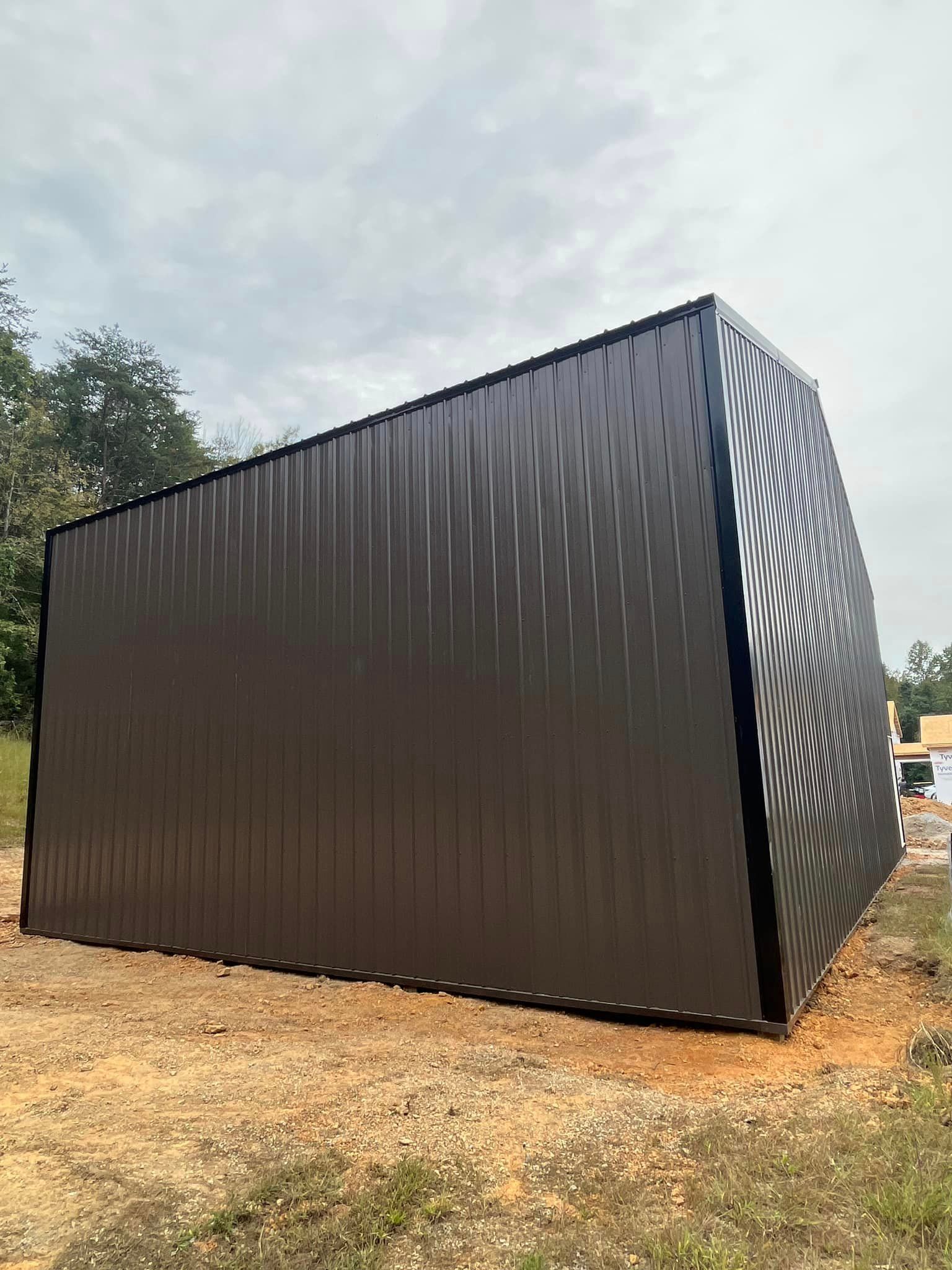 A large black metal building is sitting in the middle of a dirt field.