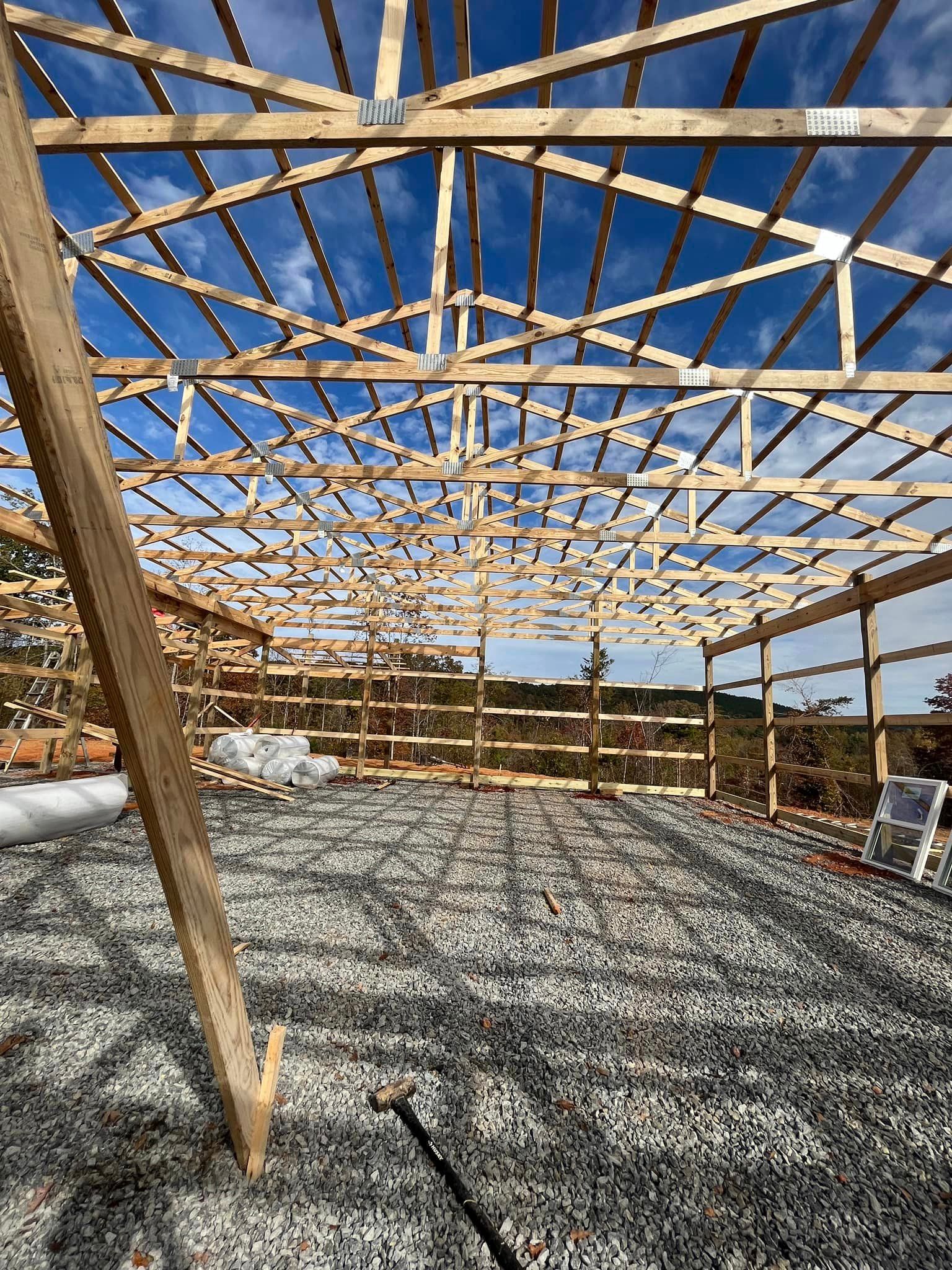 A large wooden structure is being built on a gravel lot.