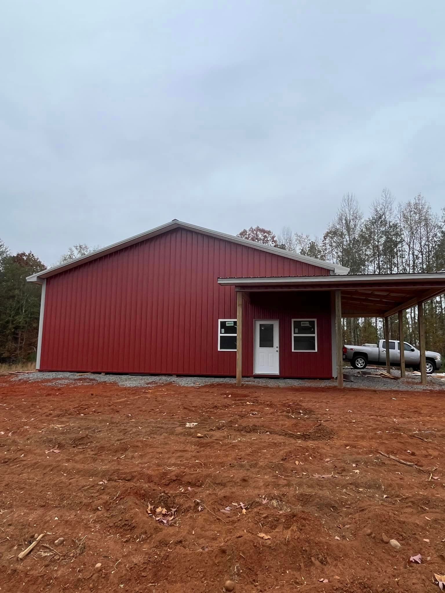 A red barn with a porch and a carport in a dirt field.