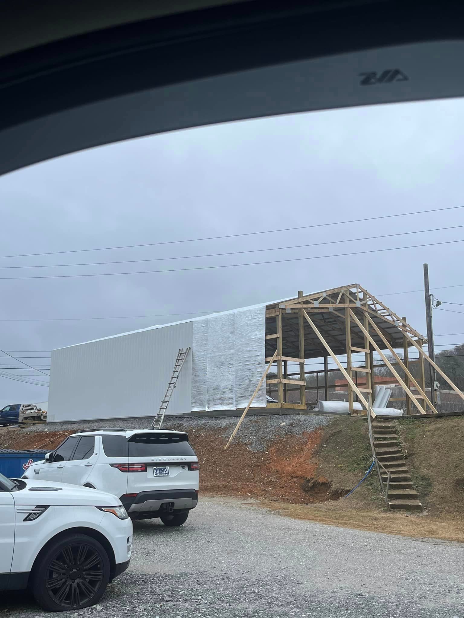 A white car is parked in front of a building under construction.