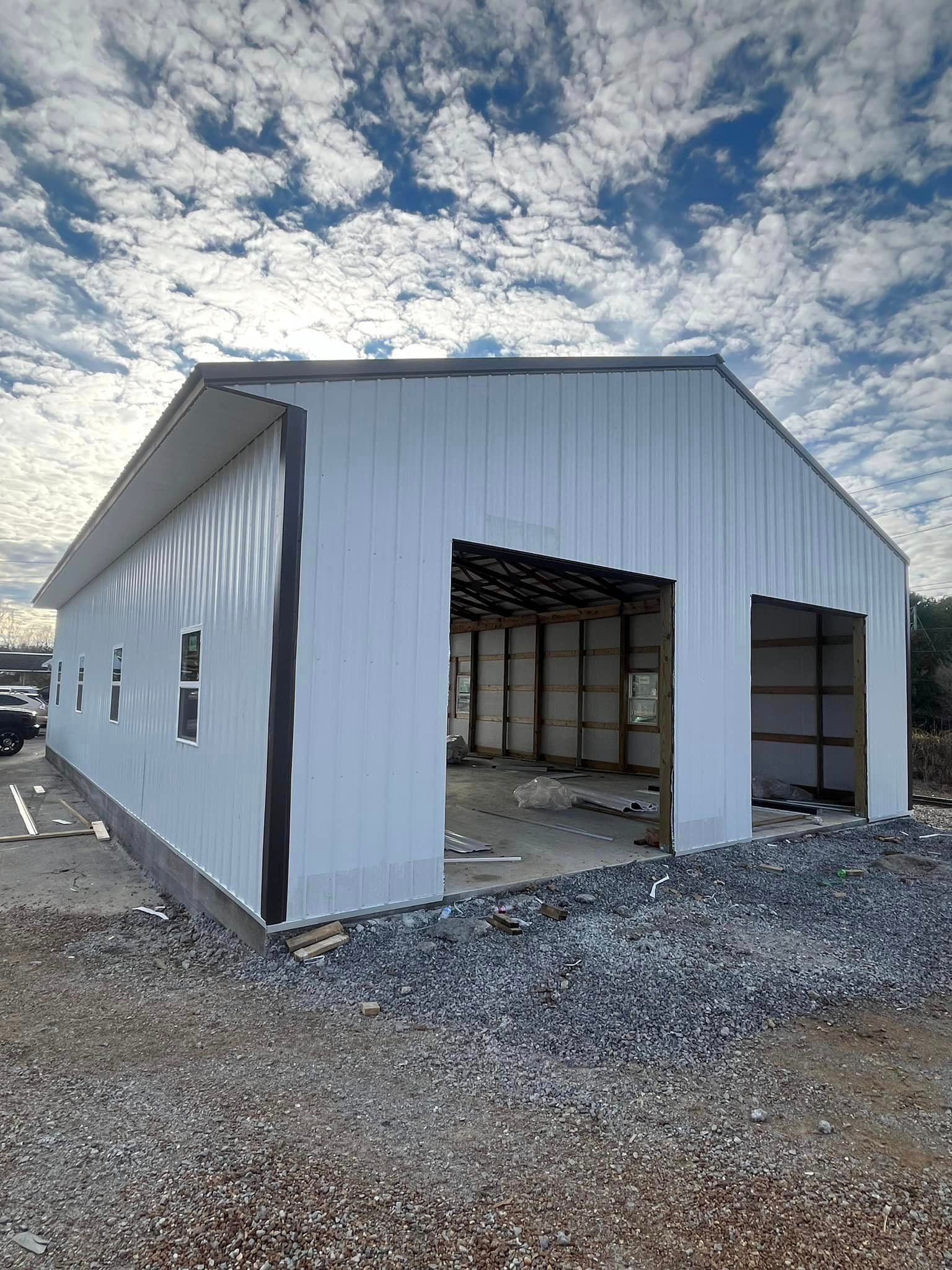 A large white metal building is being built on top of a gravel lot.