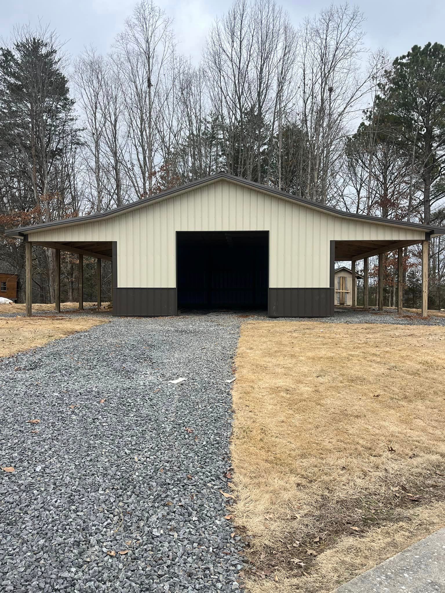 A large metal barn with a black door is sitting on top of a gravel driveway.
