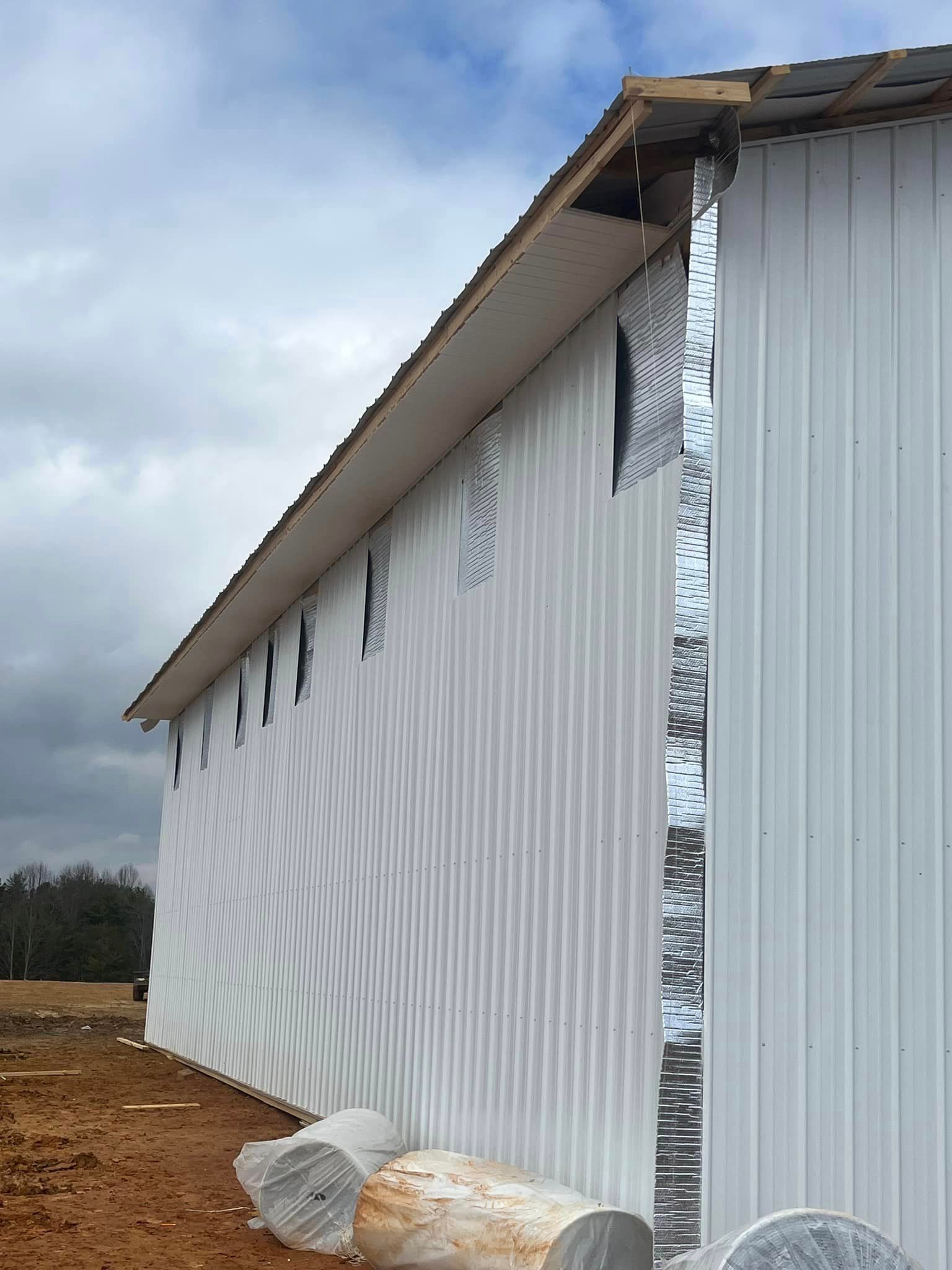 A large white building is being built on a dirt field.