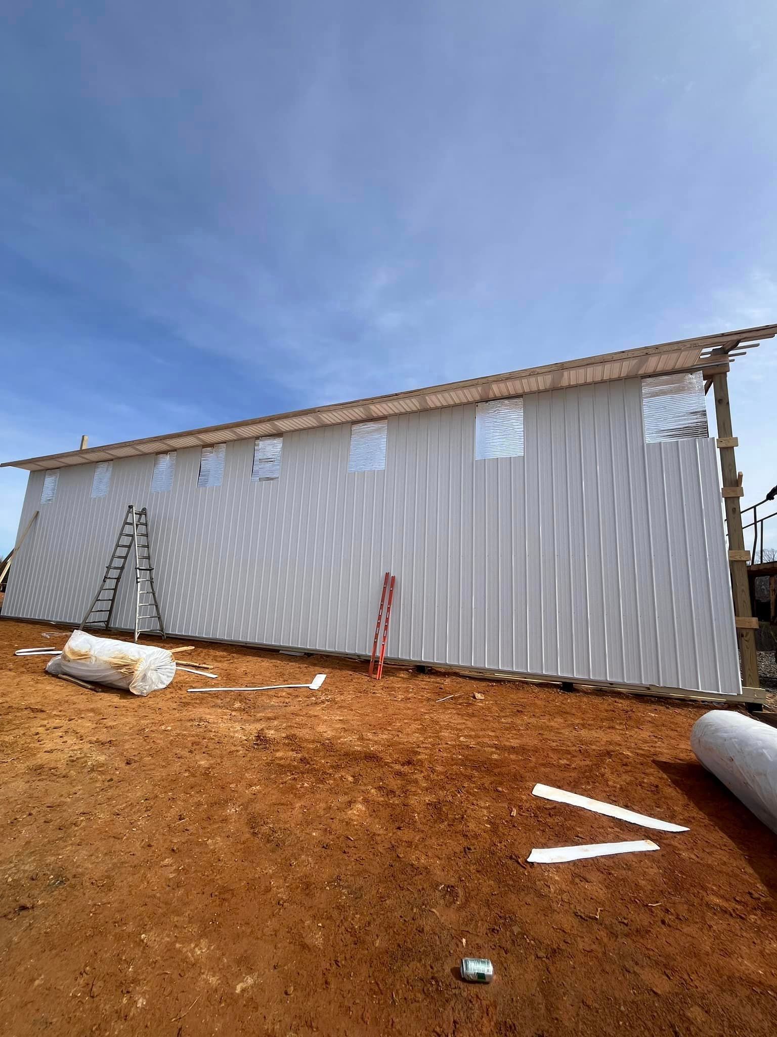 A large white building is being built in a dirt field.