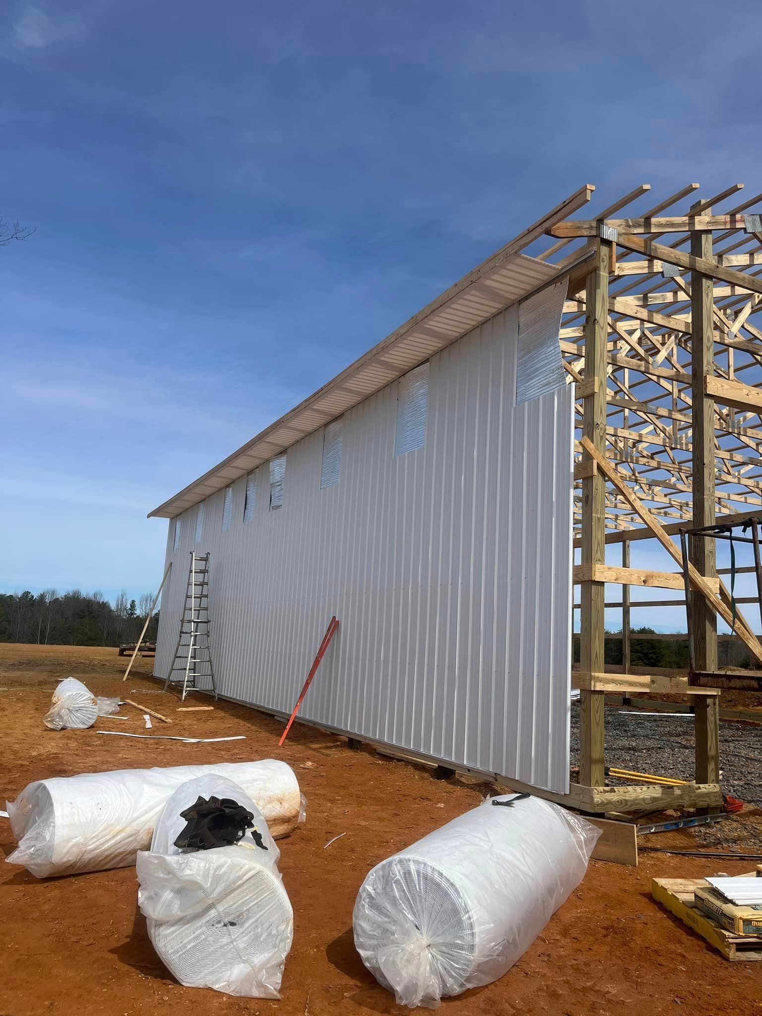 A large white barn is being built in a dirt field.