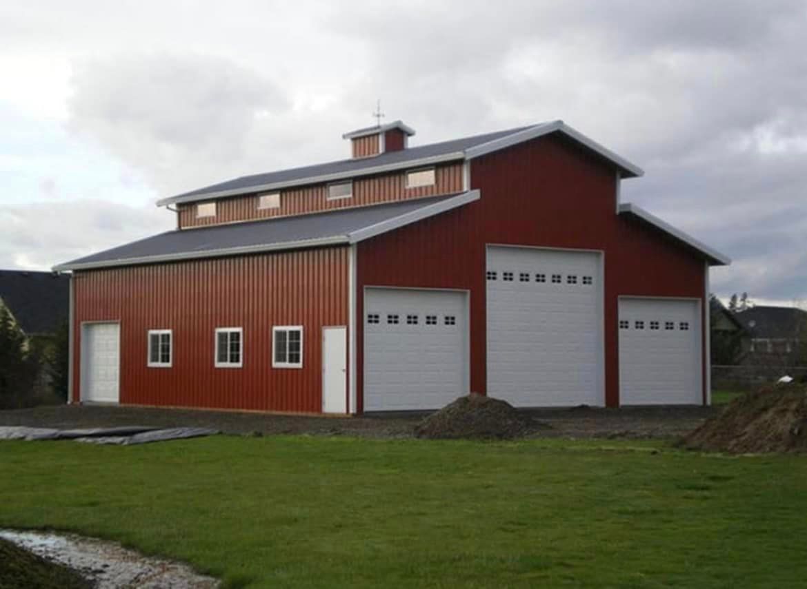 A red barn with white garage doors is in the middle of a lush green field.
