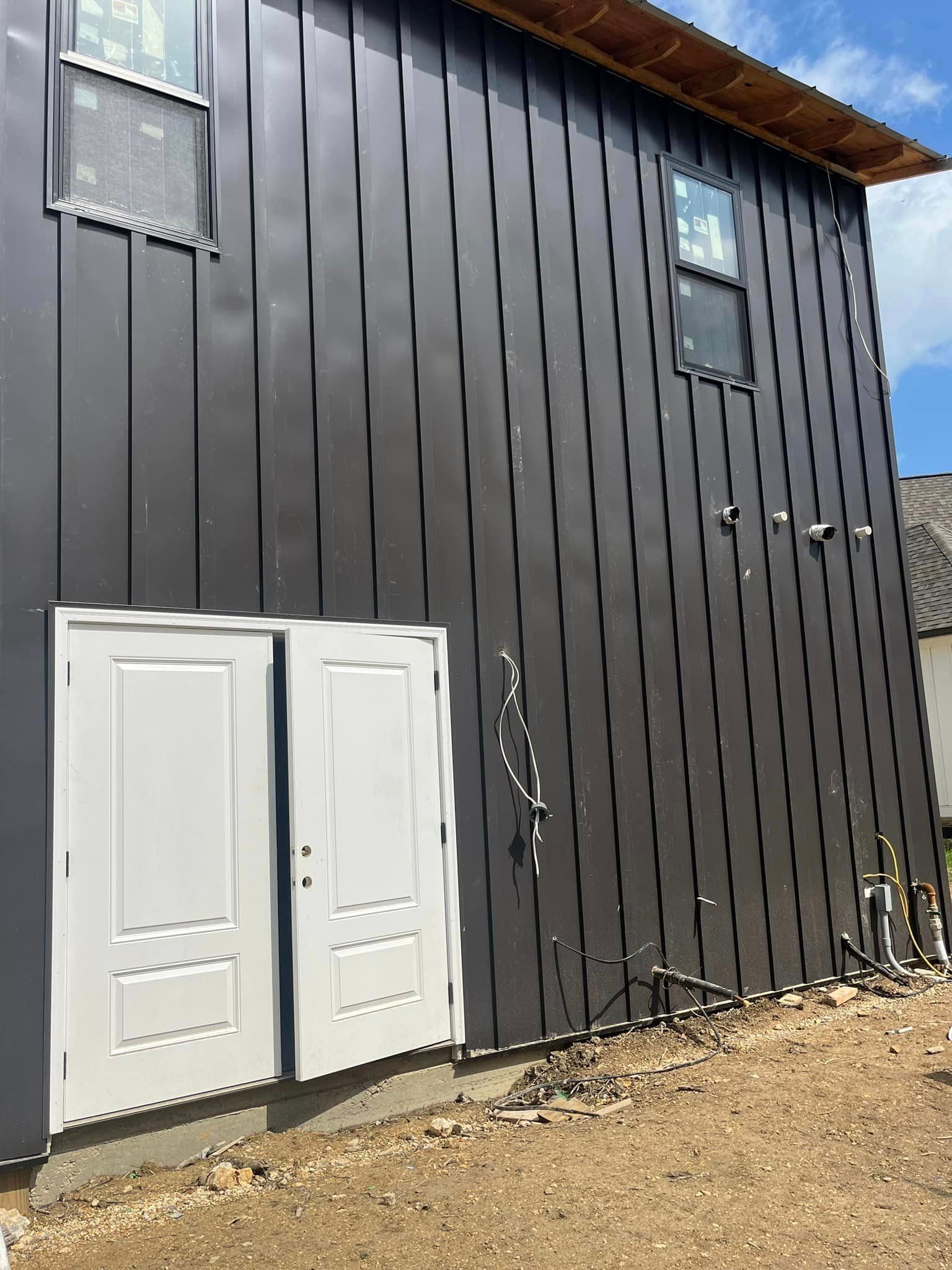 A house with a black siding and white doors is being built.