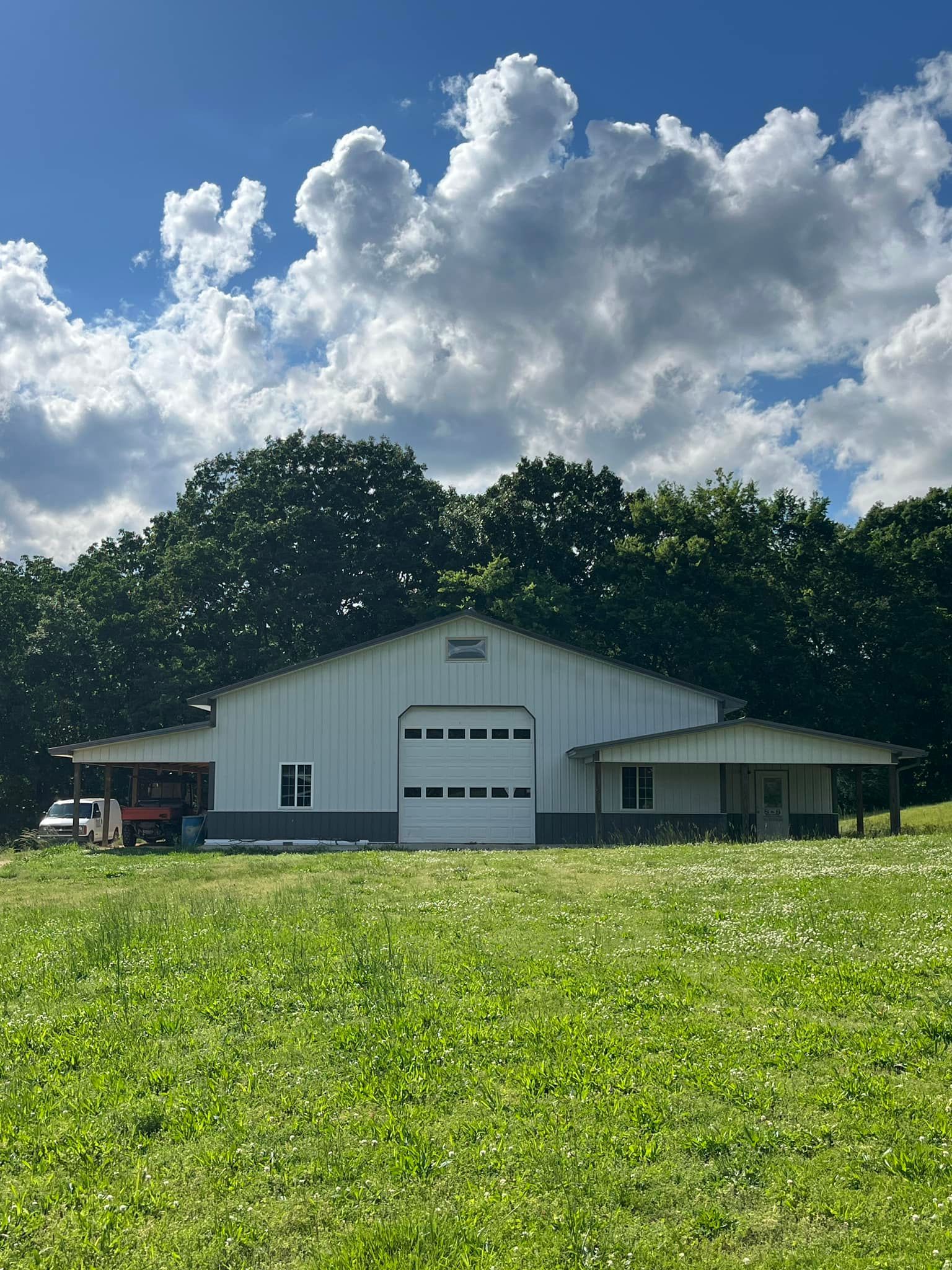 A large white barn is sitting in the middle of a grassy field.