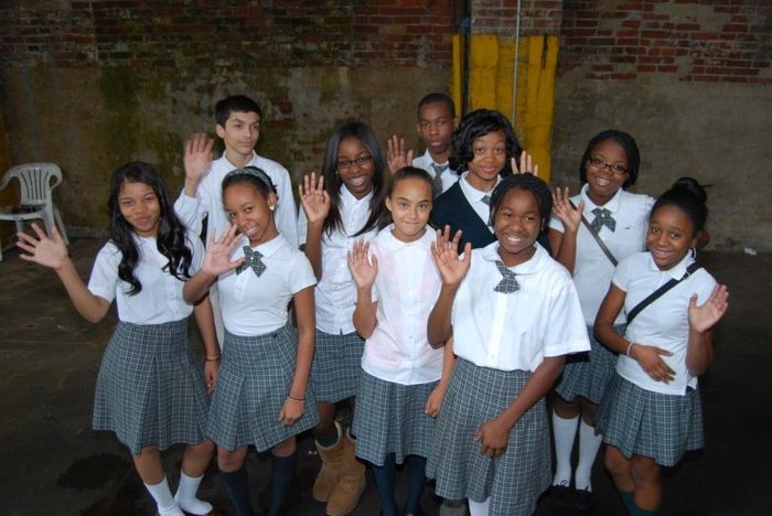 A group of children in school uniforms waving their hands