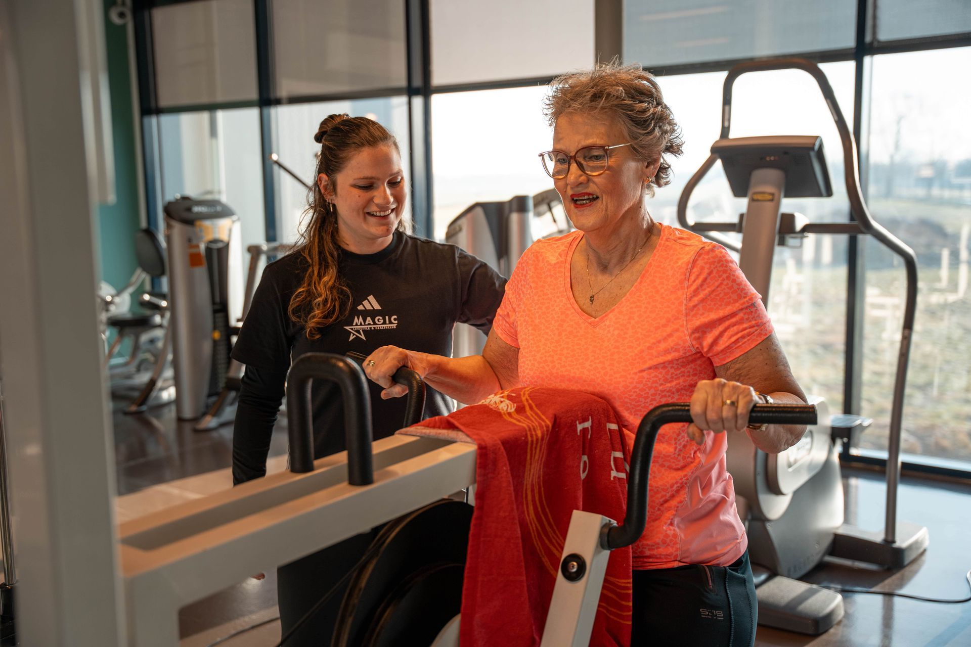 Een vrouw helpt een oudere vrouw op een loopband in een sportschool.