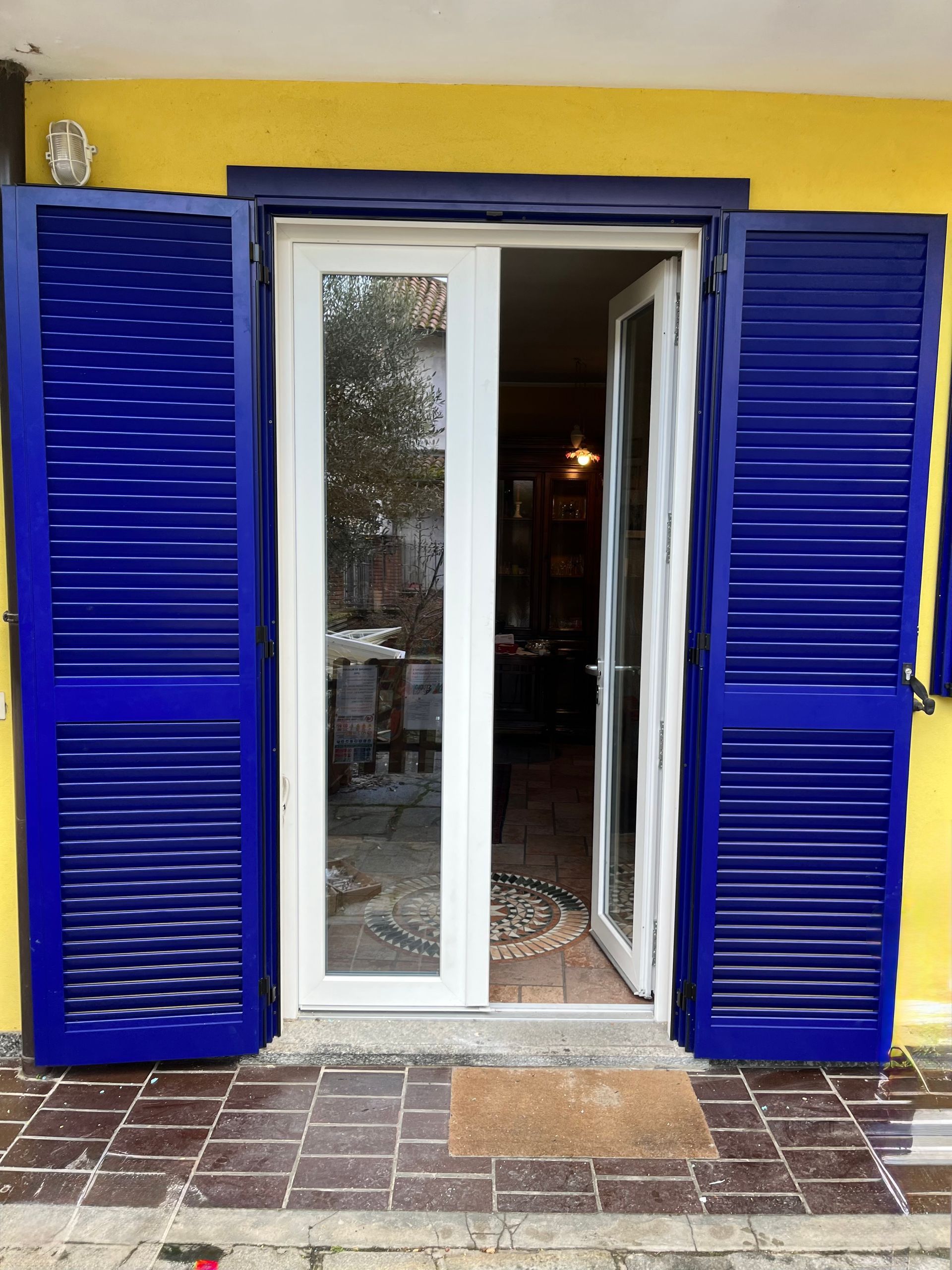 Le persiane blu incorniciano le porte-finestre bianche contro una parete gialla.