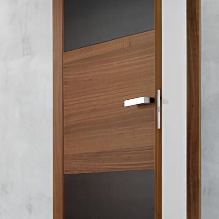 Porta in legno con pannello in legno angolato e maniglia argentata, inserita in una cornice in legno con dettagli grigio scuro e bianco.