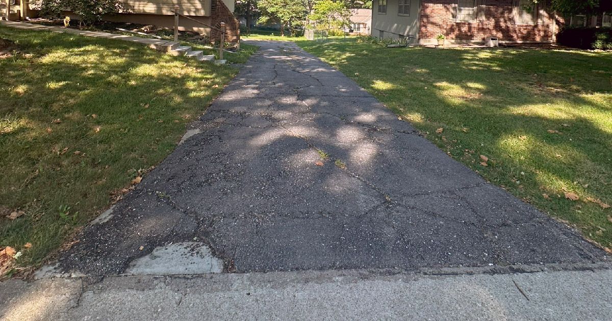 A very narrow asphalt driveway leading to a house.