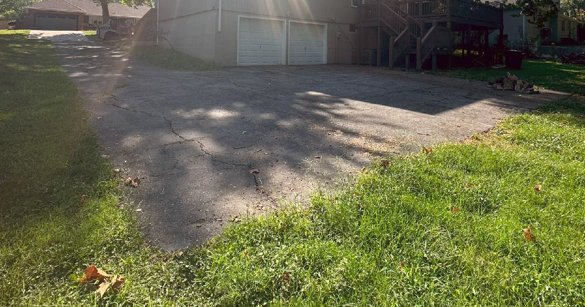 A driveway leading to a garage with a lot of grass in front of it.