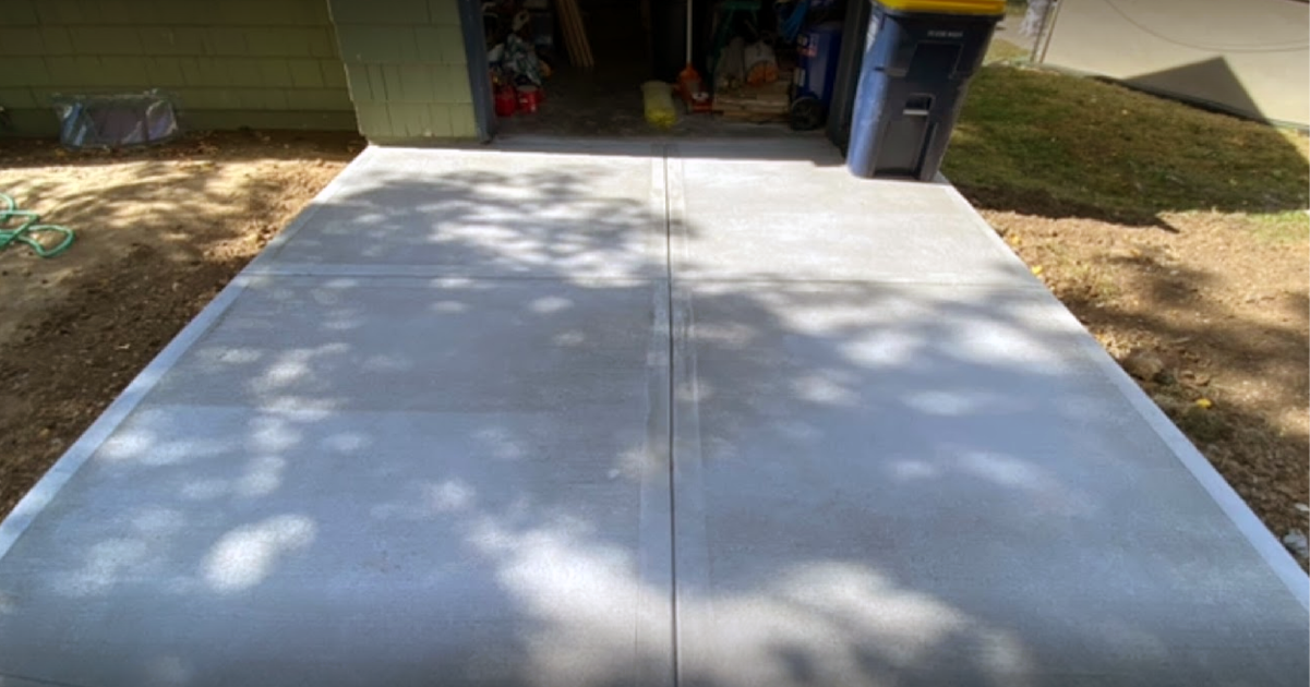 A concrete walkway leading to a garage with a trash can in the background.