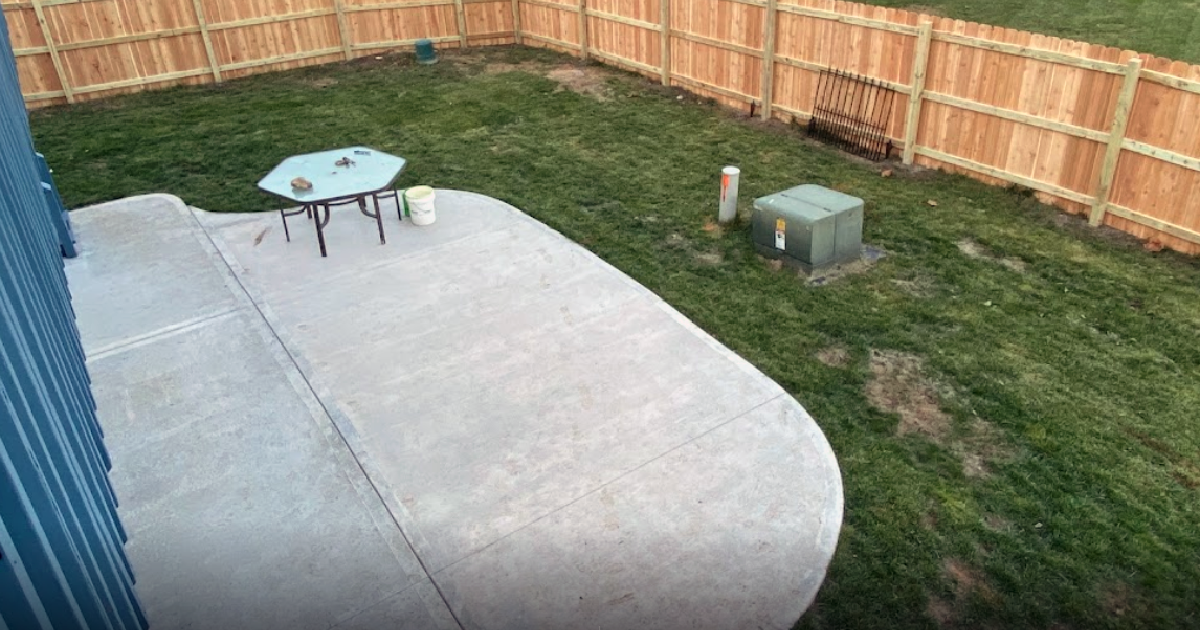 A patio with a table and chairs in a backyard with a wooden fence.