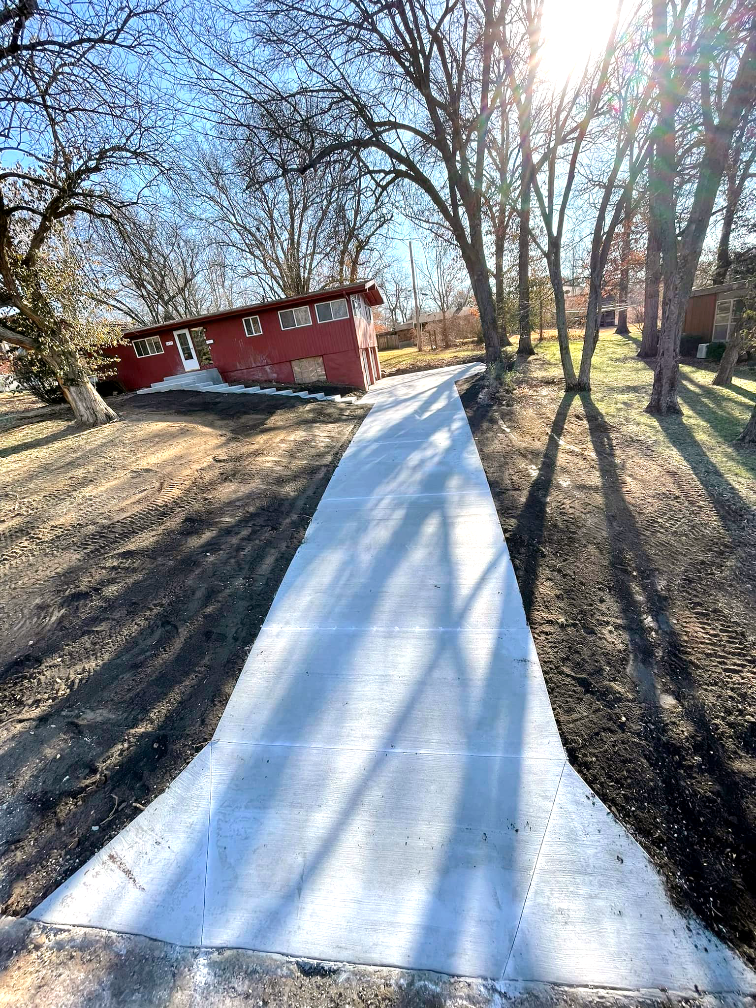 A concrete driveway leading to a red house surrounded by trees.