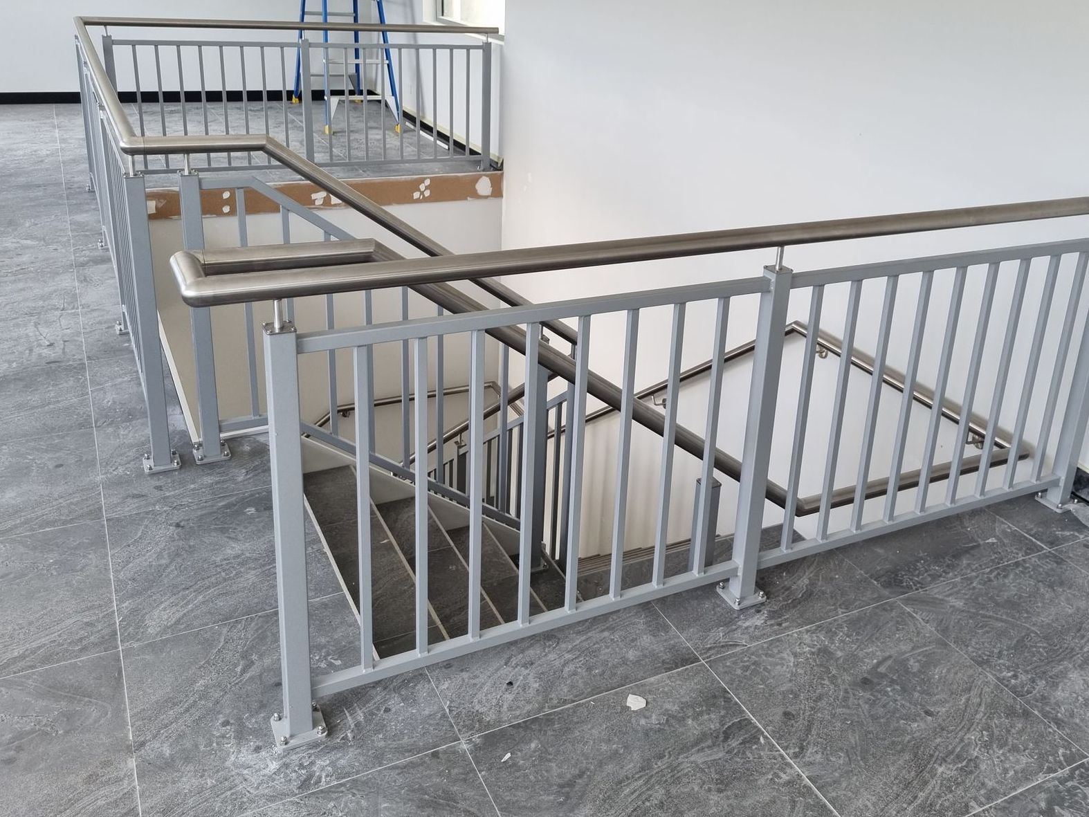 Gray metal staircase with railings and wooden handrails in a building.