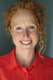 Heather with red hair and freckles is wearing a red shirt and smiling.