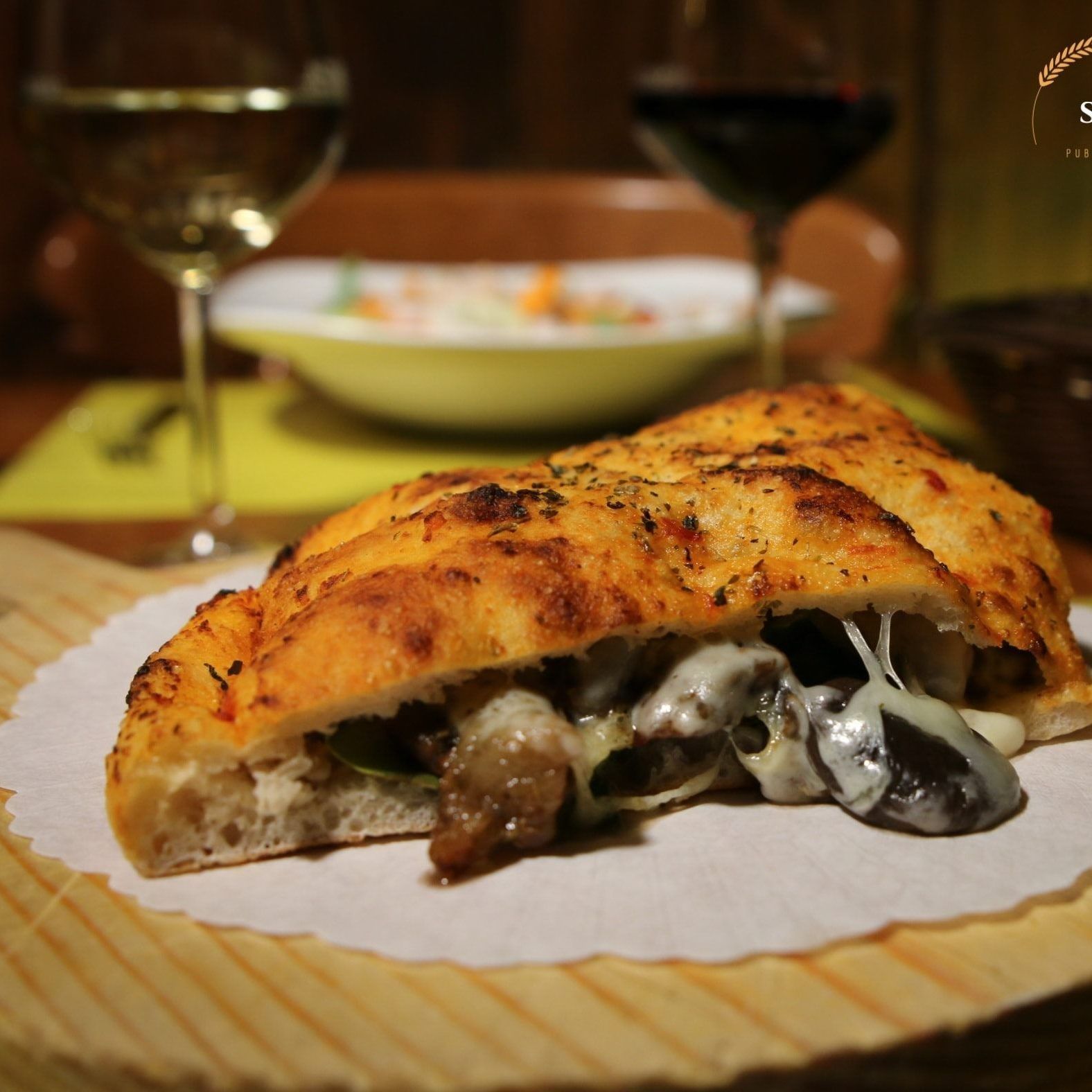 Un primo piano di una pizza su un piatto con un bicchiere di vino sullo sfondo