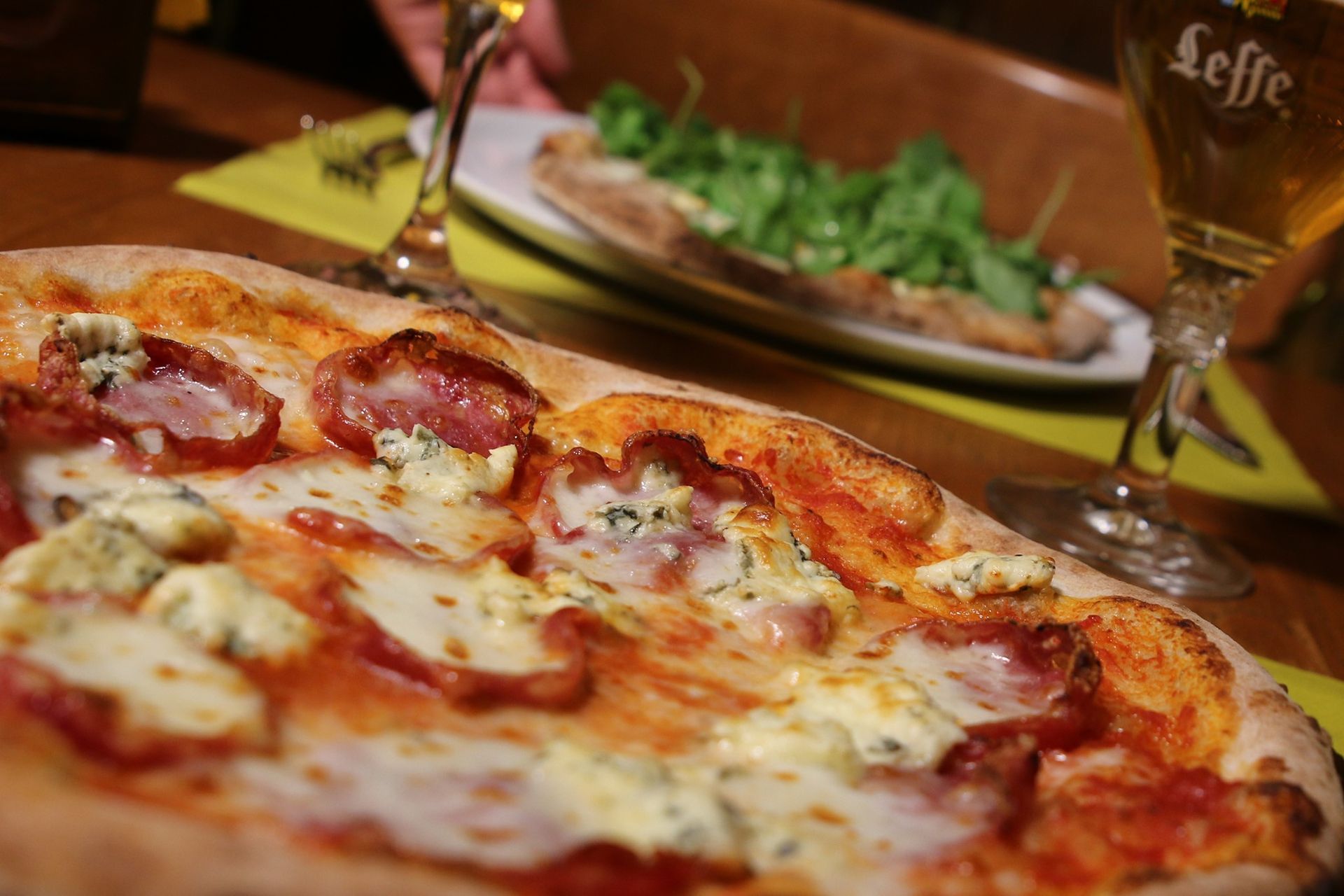 Una pizza è appoggiata su un tavolo accanto a un bicchiere di birra.