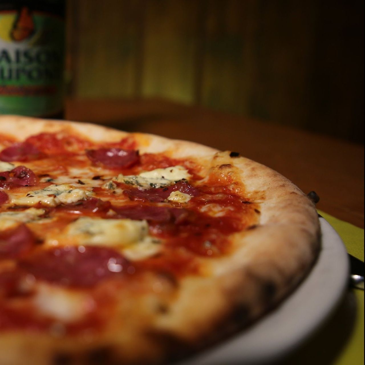 Una pizza su un piatto con una bottiglia di maison sullo sfondo