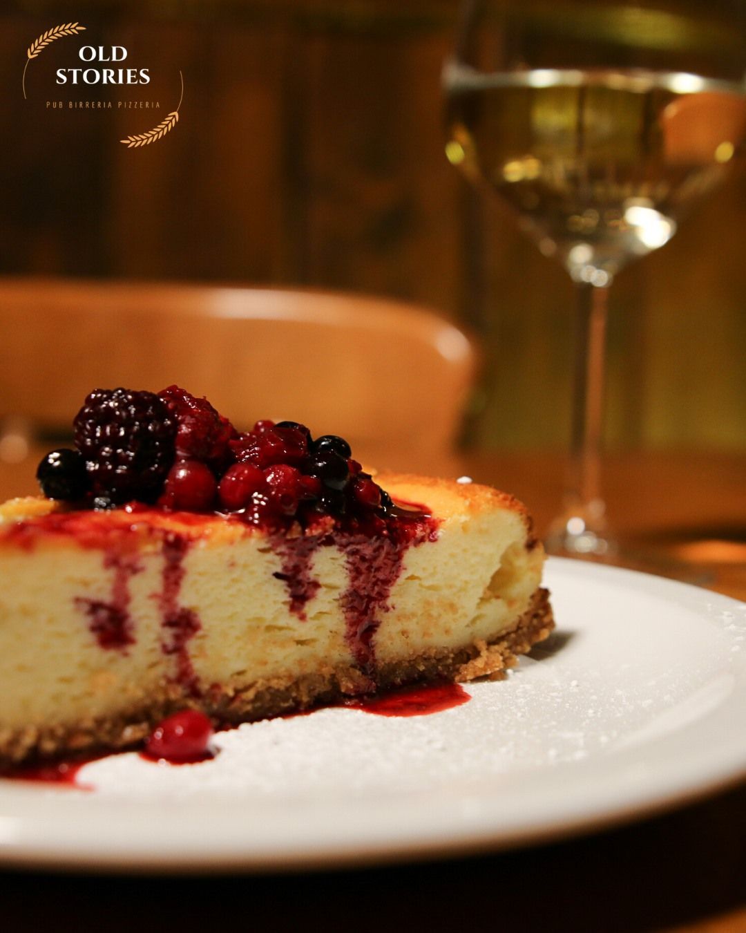 Un piatto bianco sormontato da una fetta di cheesecake e frutti di bosco accanto a un bicchiere di vino
