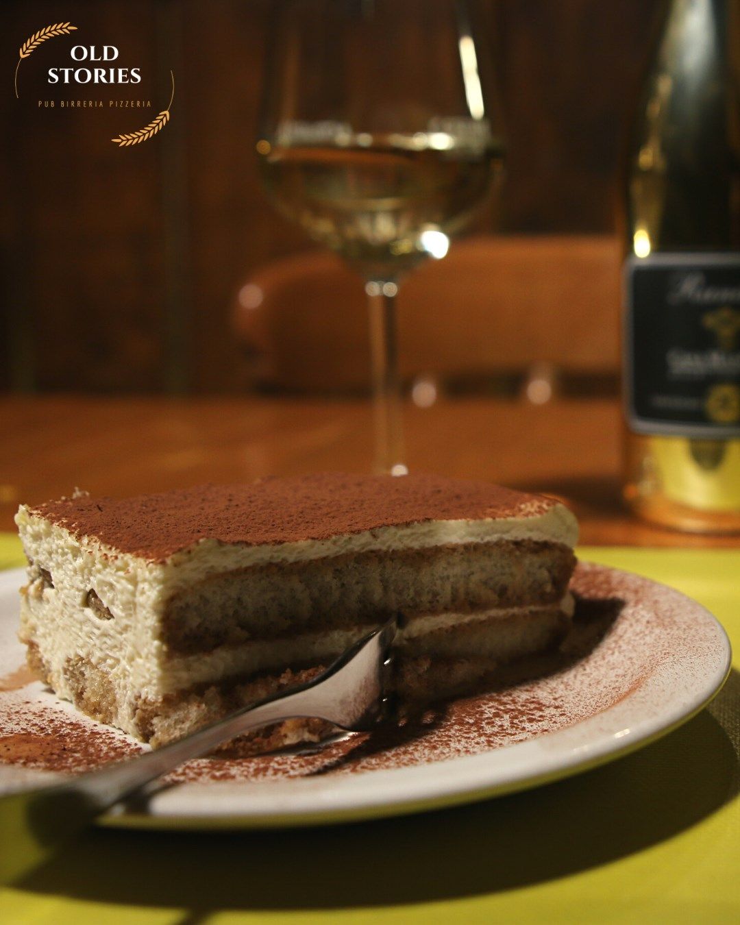 Una fetta di tiramisù è su un piatto accanto a un bicchiere di vino