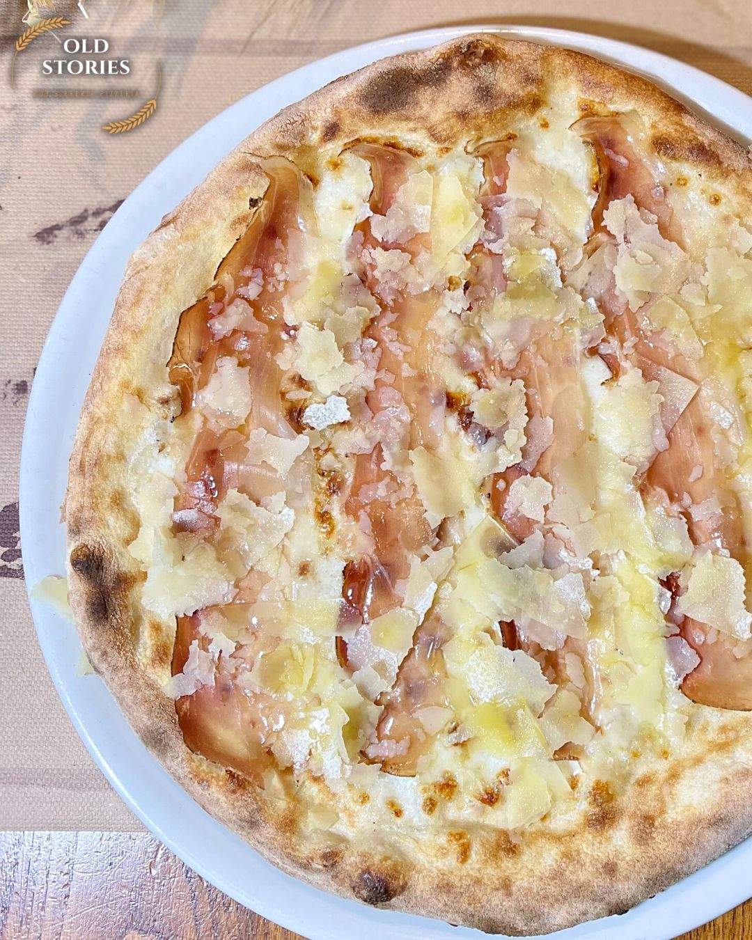Una pizza con prosciutto e formaggio è su un piatto bianco.