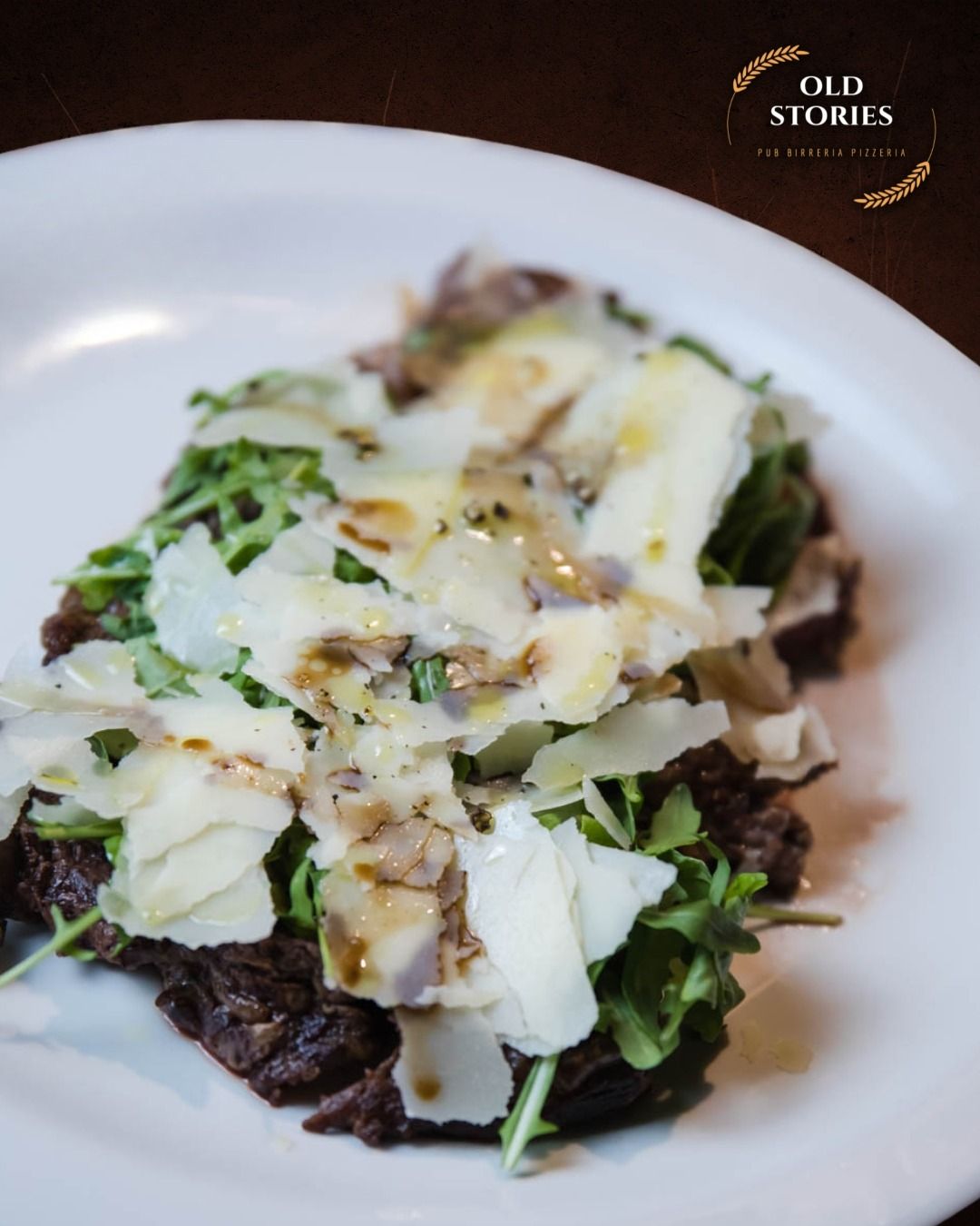 Bistecca con rucola e parmigiano grattugiato servita su un piatto bianco.