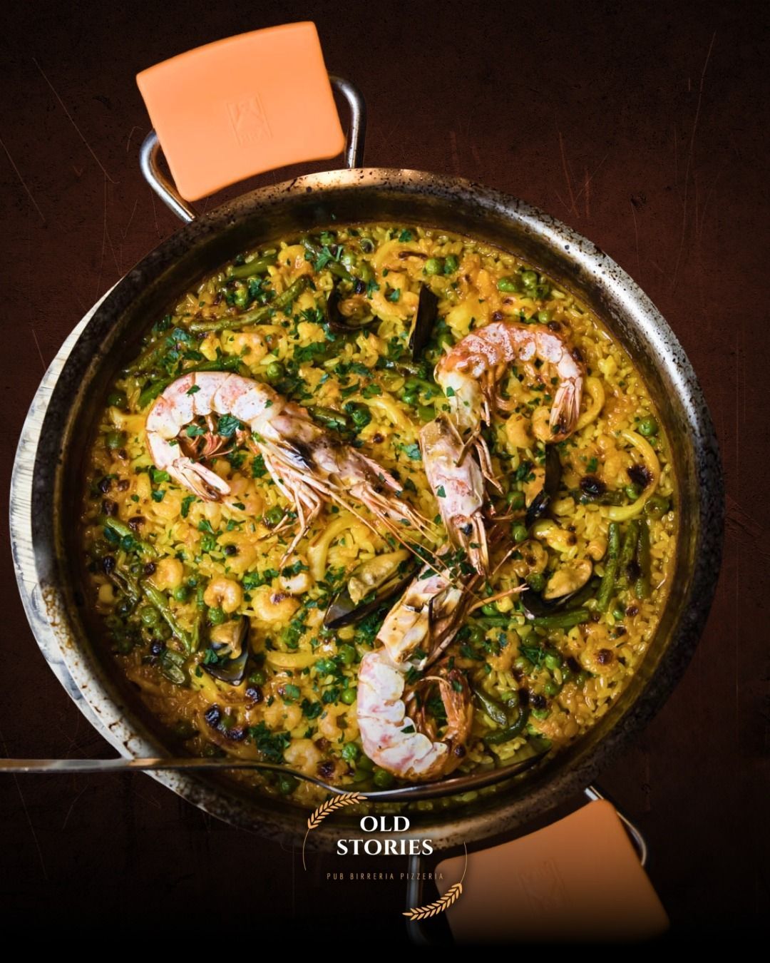 Paella con gamberi e cozze in una grande padella di metallo; erbe aromatiche, riso giallo.