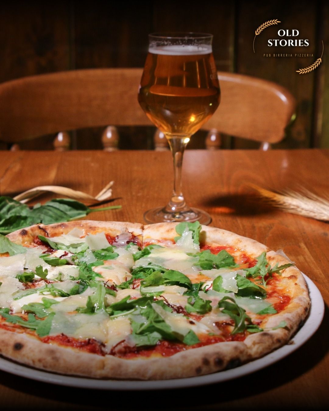 Pizza con rucola e parmigiano, un bicchiere di birra, su un tavolo di legno.