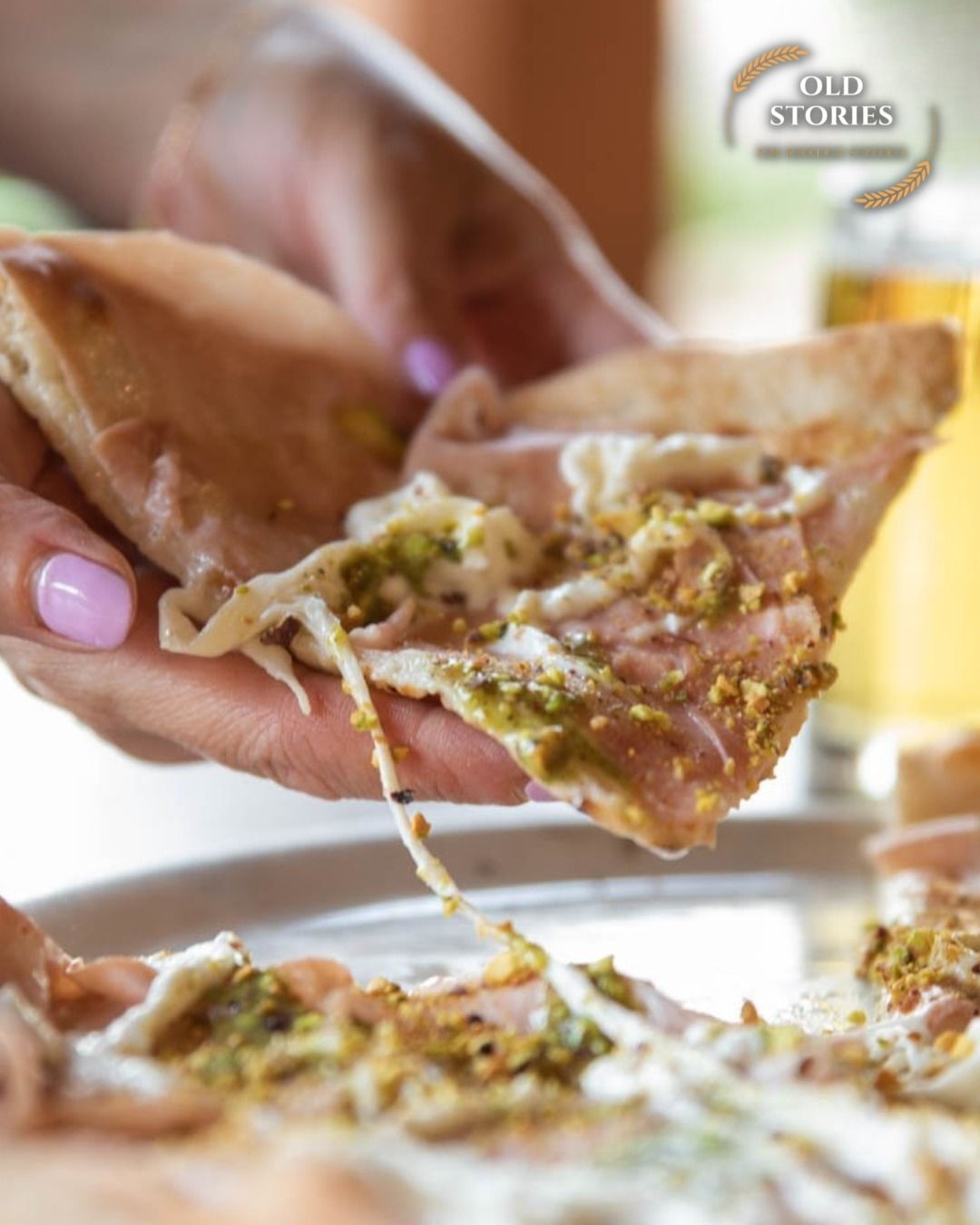 Persona che tiene in mano una fetta di pizza con condimenti visibili: prosciutto, pesto e formaggio.