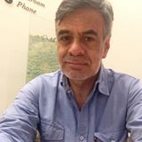 Un hombre con una camisa azul está sentado en una mesa tomándose una selfie.