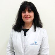Una mujer con una bata de laboratorio blanca está parada frente a una pared blanca.