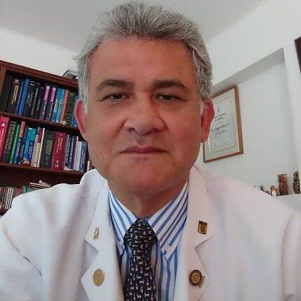 Un hombre con bata blanca y corbata mira a la cámara.