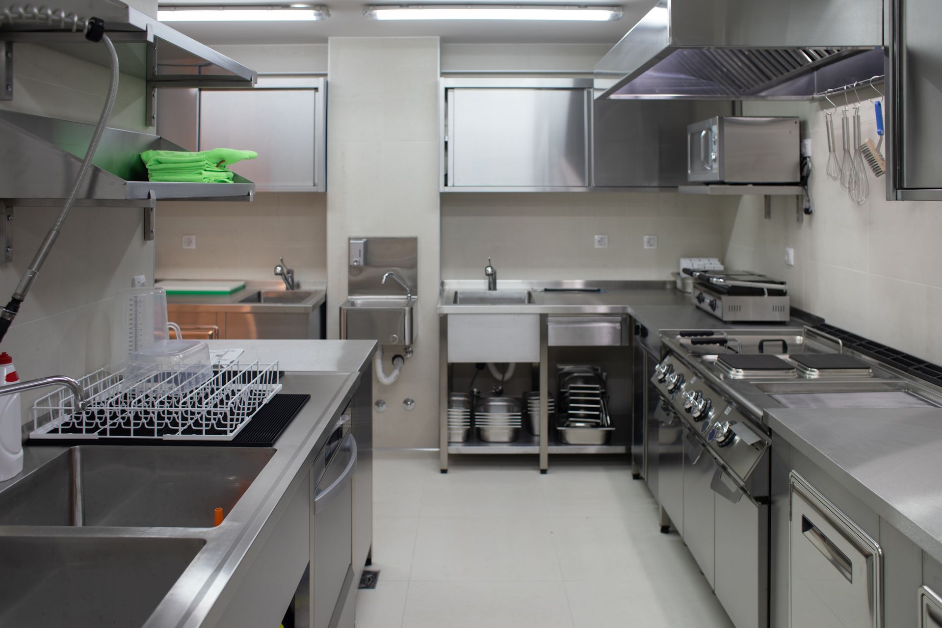 A commercial kitchen with stainless steel appliances, sinks, counters, and storage