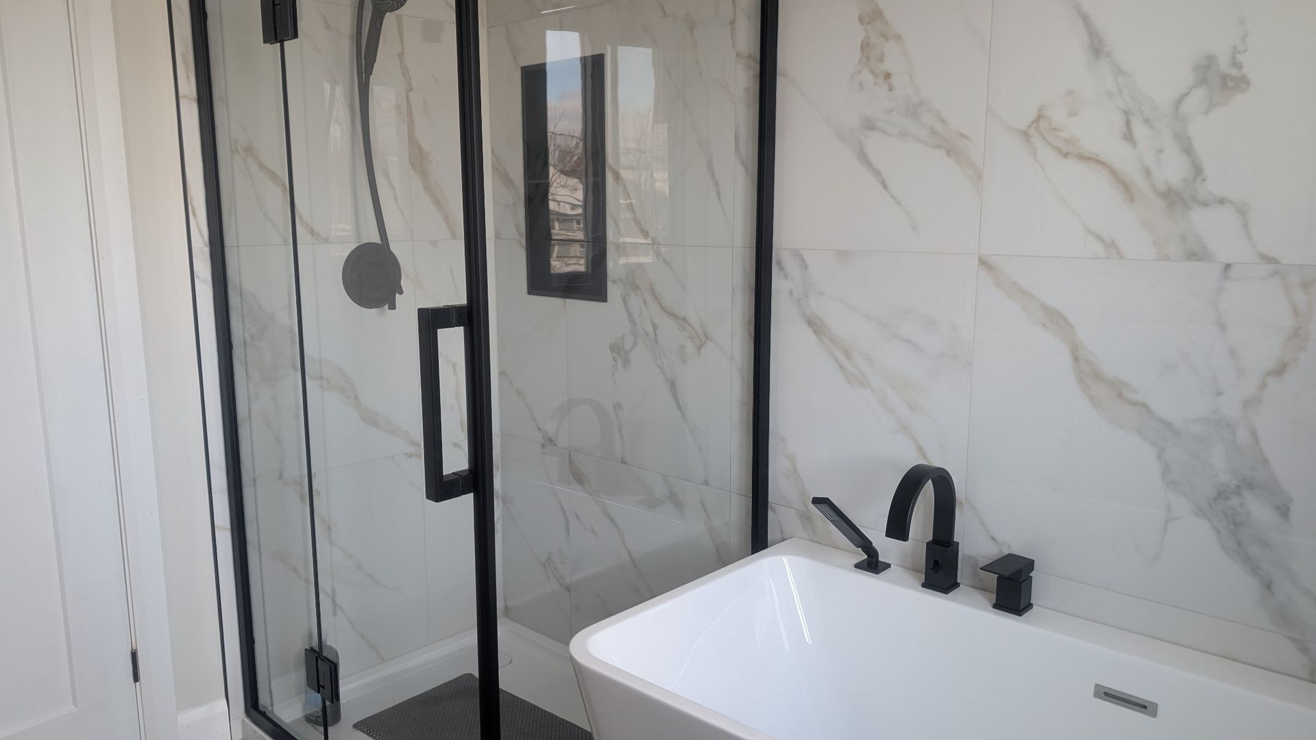 Une salle de bain avec baignoire, douche et porte de douche noire.