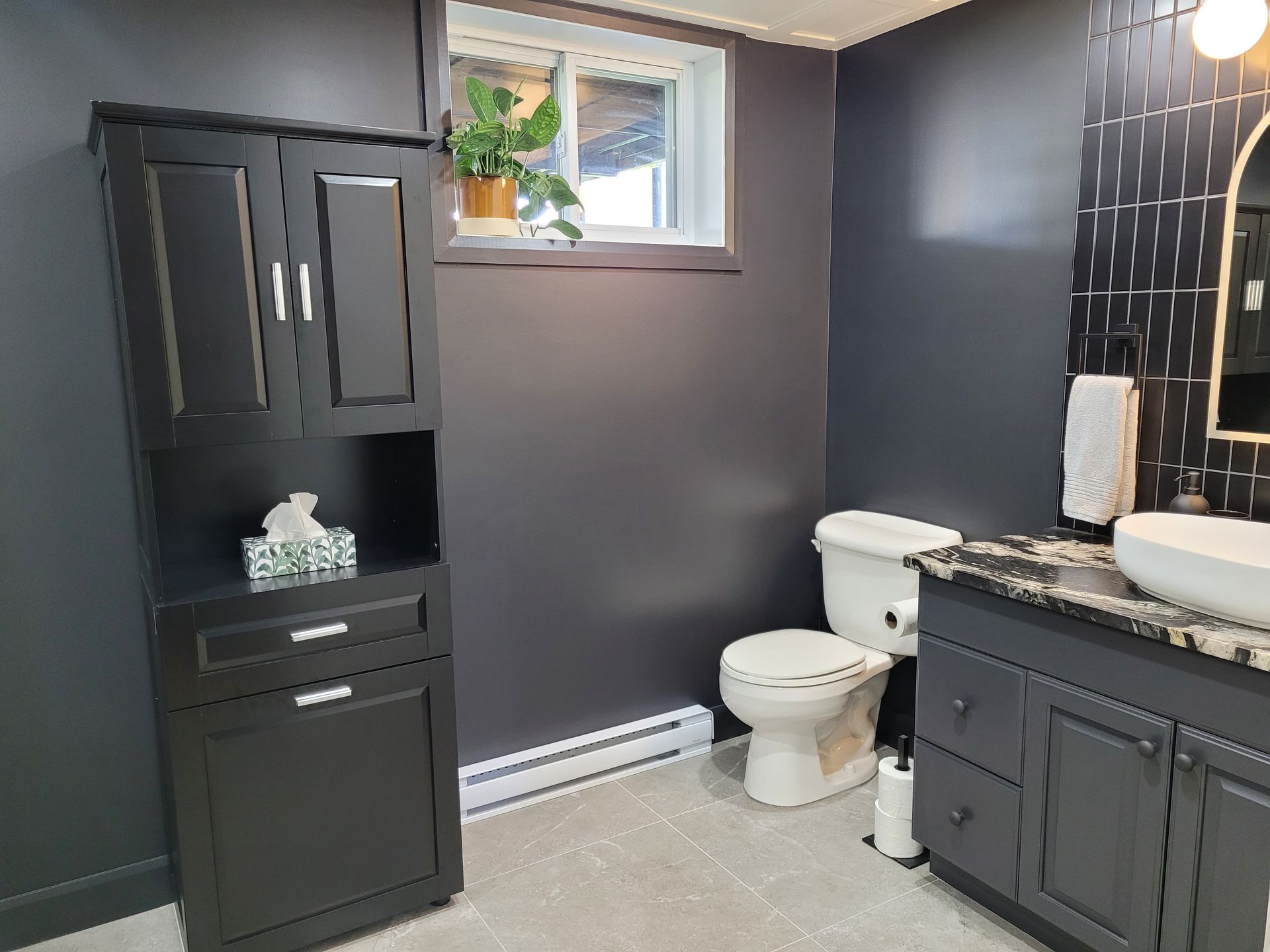 Une salle de bain avec toilettes, lavabo, armoires et une fenêtre.