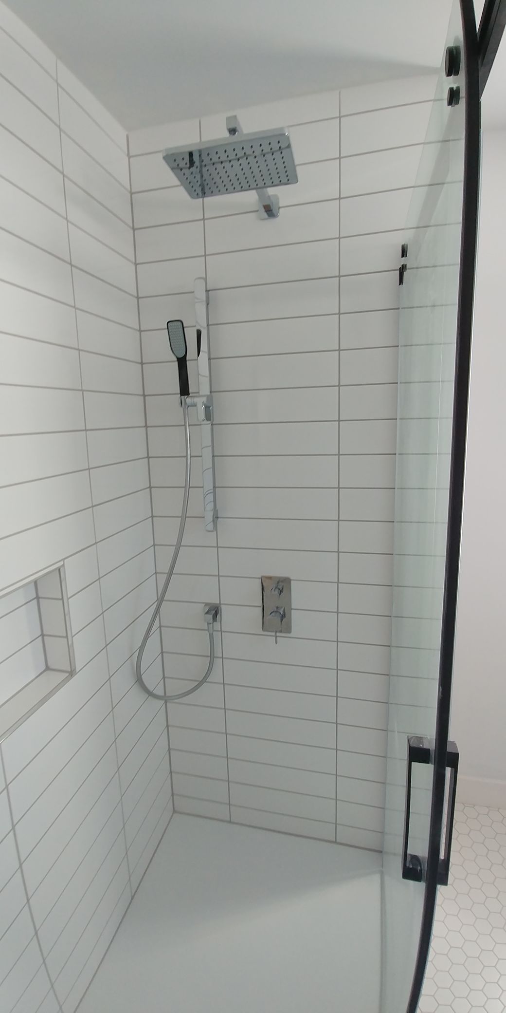 Une salle de bain avec carrelage blanc et une douche à l'italienne avec porte vitrée.