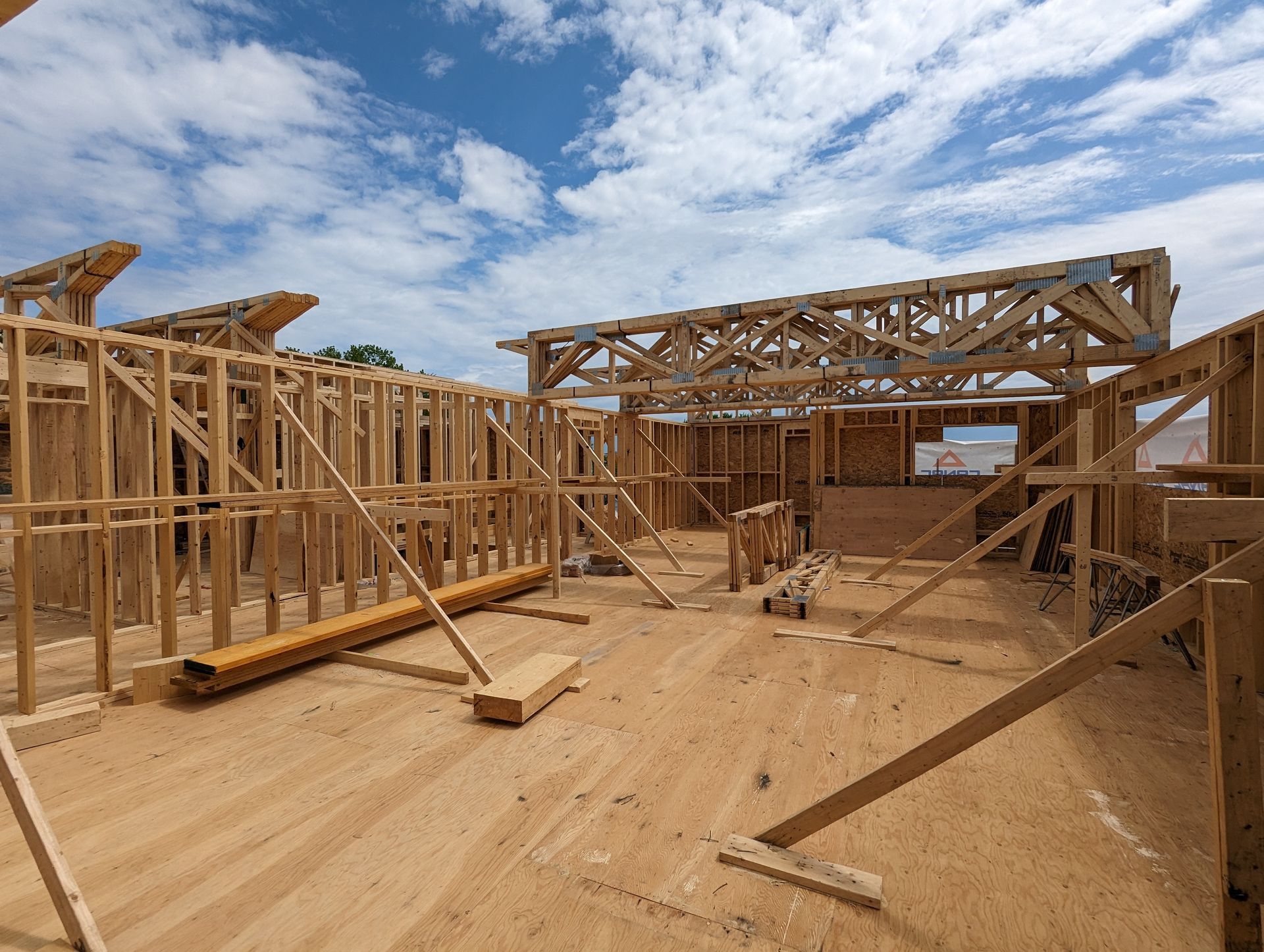 Une maison est en construction avec des poutres en bois et un ciel bleu en arrière-plan.