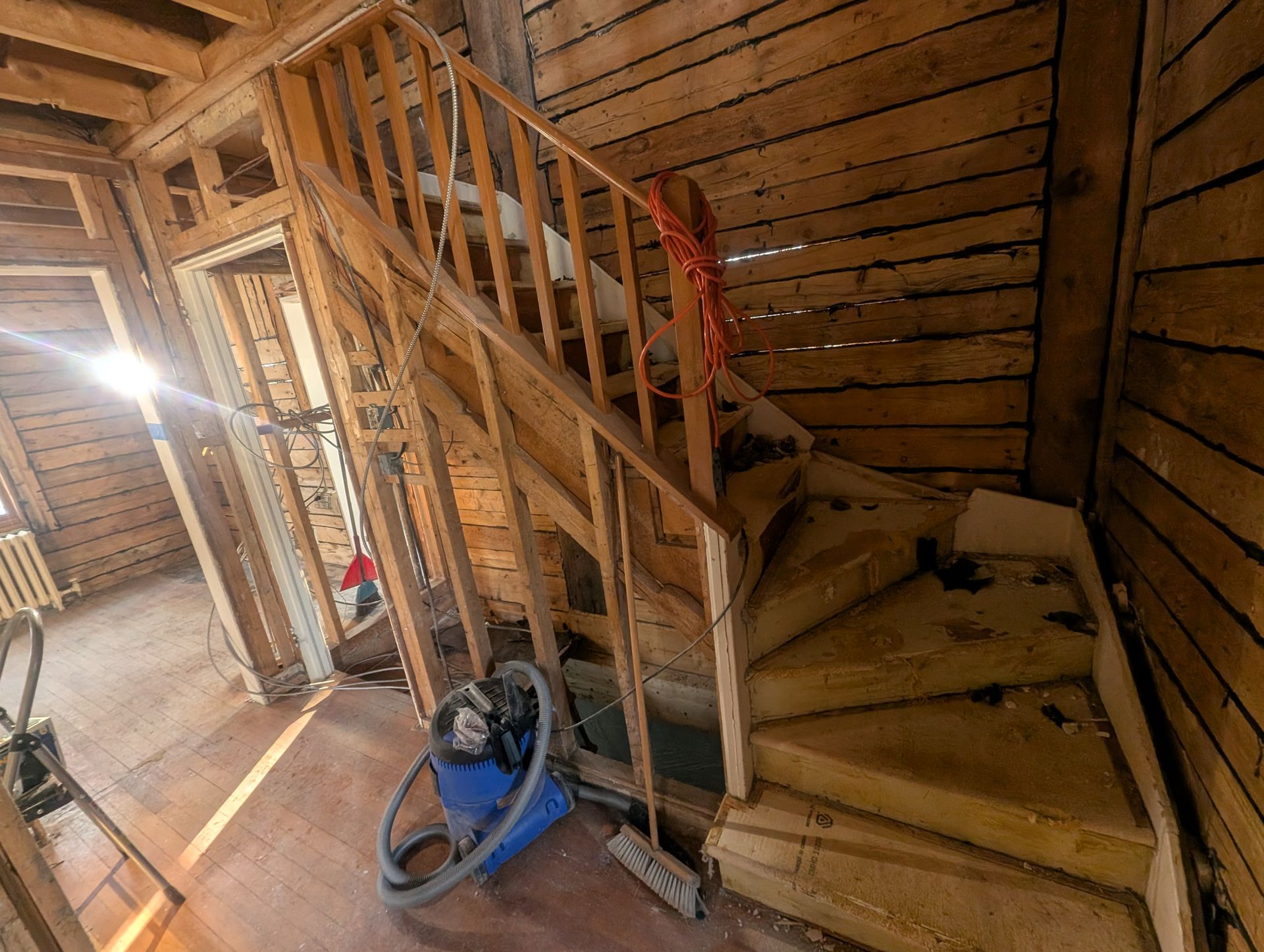 Un aspirateur est posé sur le sol à côté d'un escalier en bois.