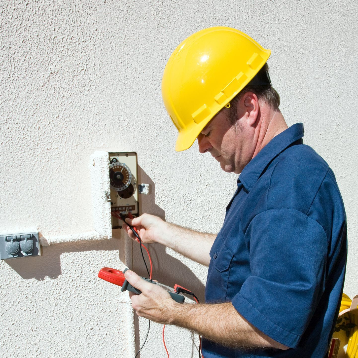A man wearing a yellow hard hat is working on an electrical box