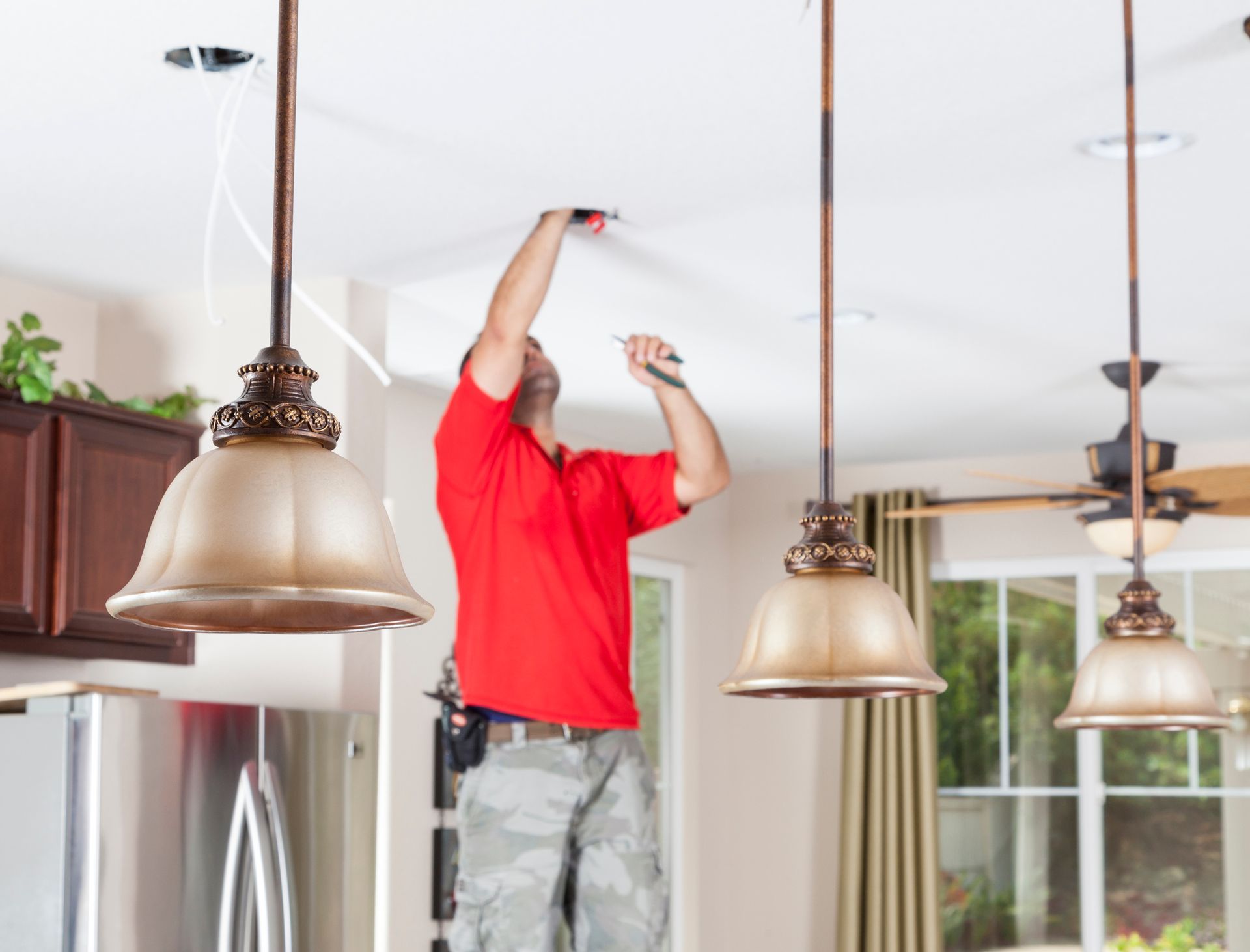 A man in a red shirt is working on a ceiling light