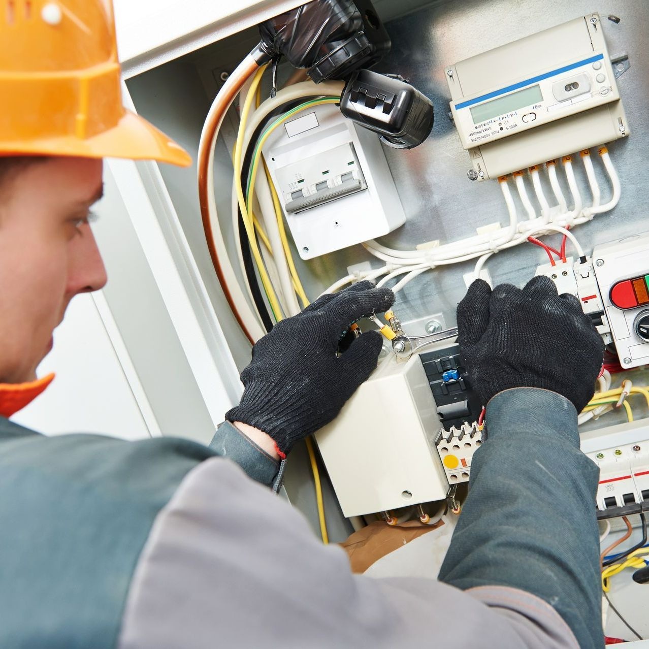A man wearing a hard hat is working on an electrical box