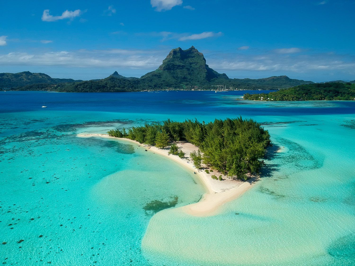 Aerial view of a small tropical island with a white sand beach, surrounded by turquoise water, with a mountain in back. Aerial view of a small tropical island with a white sand beach, surrounded by turquoise water, with a mountain in back.
